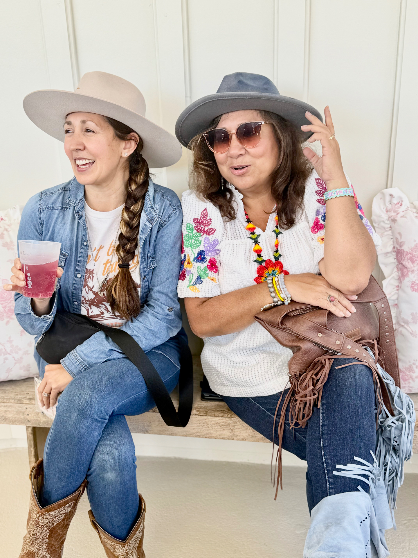 Two smiling women in hats enjoying a drink together in Burton, Texas